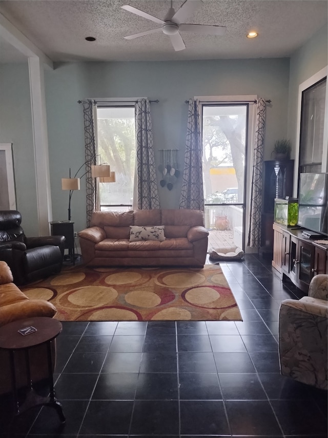 living room featuring ceiling fan, a textured ceiling, and dark tile patterned flooring