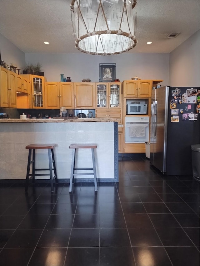 kitchen featuring glass insert cabinets, a textured ceiling, stainless steel appliances, and dark tile patterned flooring