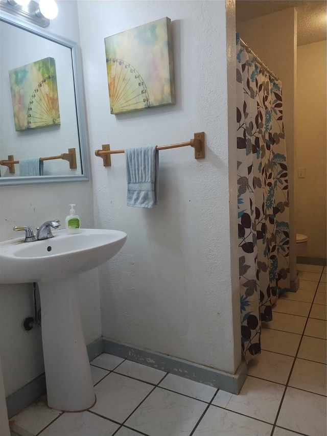 full bathroom with curtained shower, tile patterned floors, toilet, a sink, and baseboards