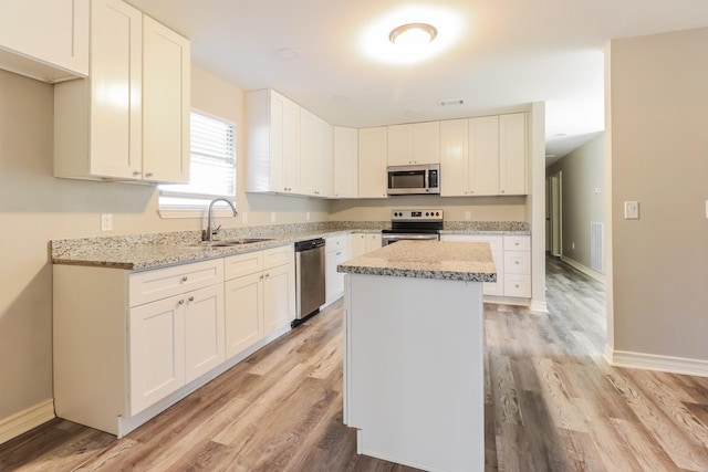 kitchen featuring a kitchen island, sink, white cabinetry, light stone countertops, and stainless steel appliances