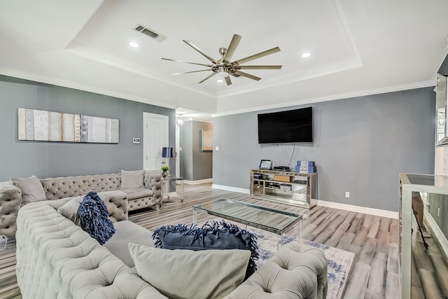 living room featuring crown molding, a raised ceiling, light hardwood / wood-style flooring, and ceiling fan