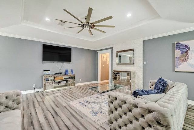 living room with a fireplace, ornamental molding, wood-type flooring, ceiling fan, and a raised ceiling