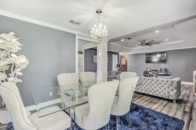 dining space featuring a raised ceiling, ceiling fan with notable chandelier, wood-type flooring, decorative columns, and ornamental molding