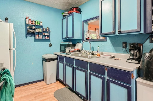 kitchen featuring sink, light hardwood / wood-style floors, a textured ceiling, white fridge, and blue cabinetry