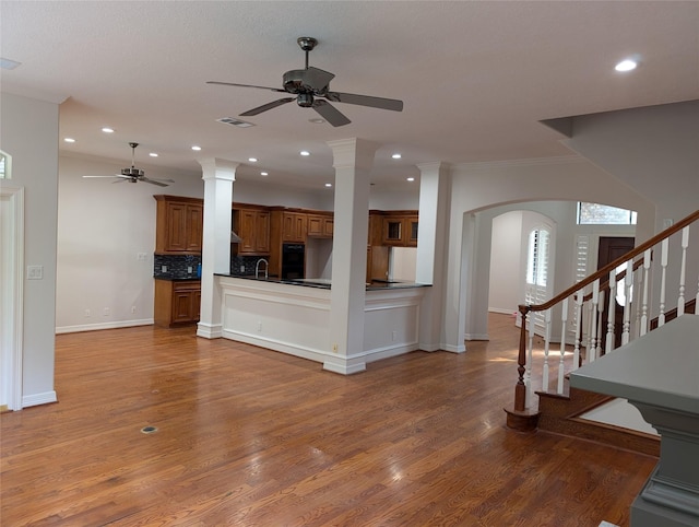 unfurnished living room featuring decorative columns, wood-type flooring, sink, and ceiling fan