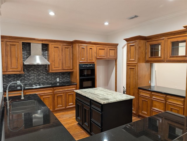 kitchen featuring wall chimney range hood, sink, double oven, a center island, and stainless steel gas stovetop