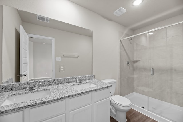 bathroom featuring a shower with shower door, toilet, double sink vanity, and hardwood / wood-style floors