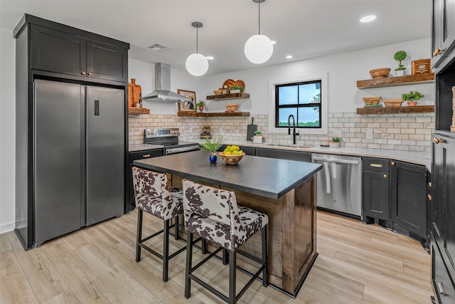 kitchen with a center island, backsplash, wall chimney exhaust hood, appliances with stainless steel finishes, and sink