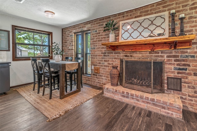 dining space with brick wall, a textured ceiling, a brick fireplace, and wood-type flooring