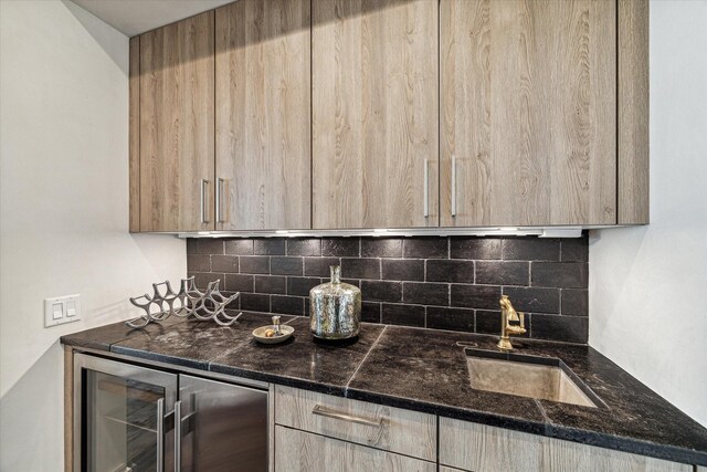 kitchen featuring dark stone counters, beverage cooler, sink, and tasteful backsplash