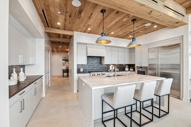 kitchen featuring appliances with stainless steel finishes, decorative backsplash, custom exhaust hood, decorative light fixtures, and sink