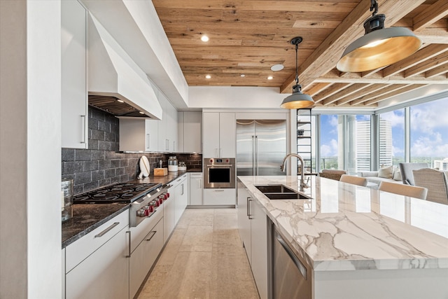 kitchen with white cabinets, custom exhaust hood, decorative light fixtures, appliances with stainless steel finishes, and a spacious island