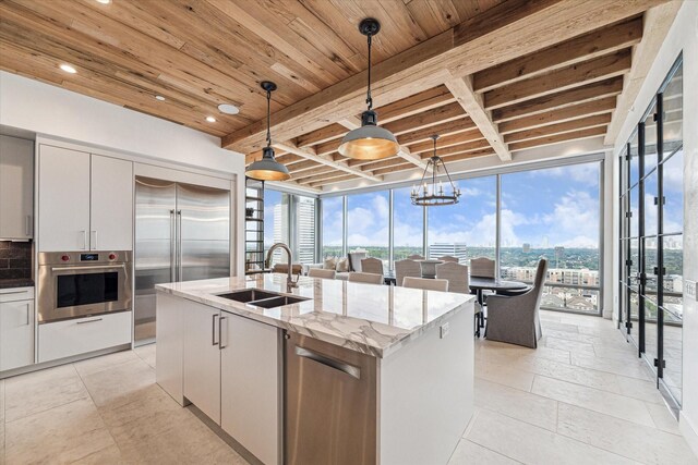 kitchen featuring white cabinetry, an island with sink, stainless steel appliances, decorative light fixtures, and sink