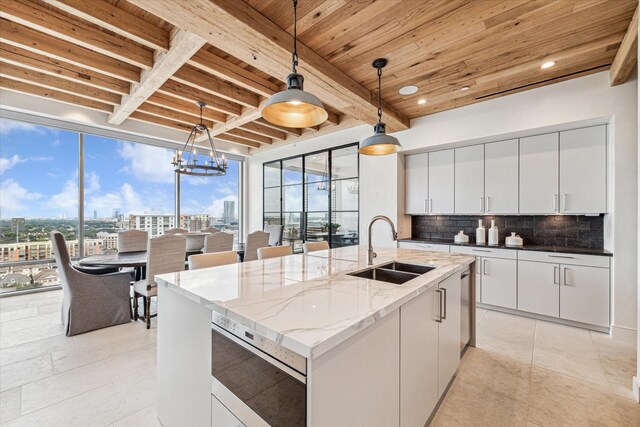 kitchen featuring a chandelier, sink, an island with sink, white cabinets, and decorative light fixtures