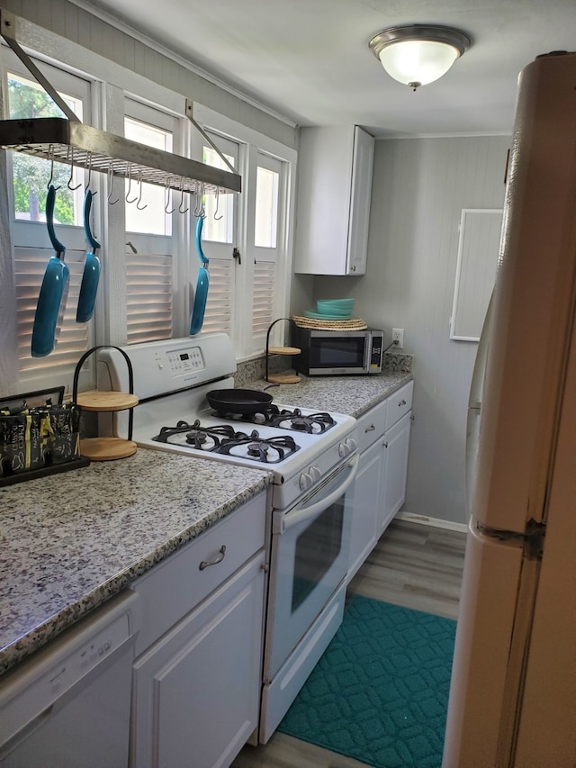 kitchen with a wealth of natural light, white cabinets, light stone counters, and white appliances