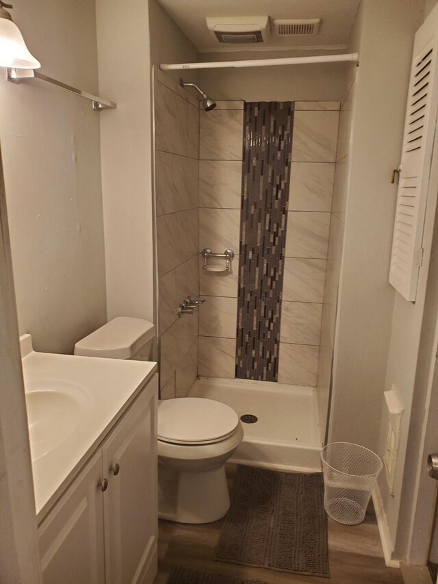 bathroom with toilet, vanity, wood-type flooring, and tiled shower