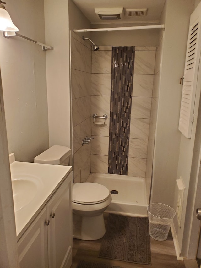 bathroom featuring hardwood / wood-style floors, vanity, toilet, and tiled shower