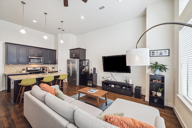 living room featuring ceiling fan, a wealth of natural light, a high ceiling, and dark wood-type flooring