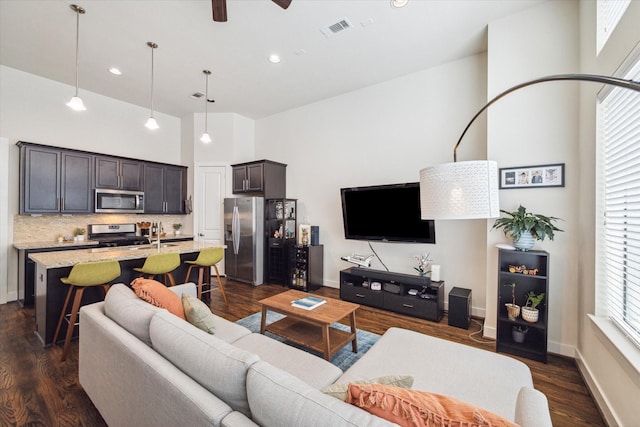 living room with dark wood-type flooring, ceiling fan, sink, and a towering ceiling