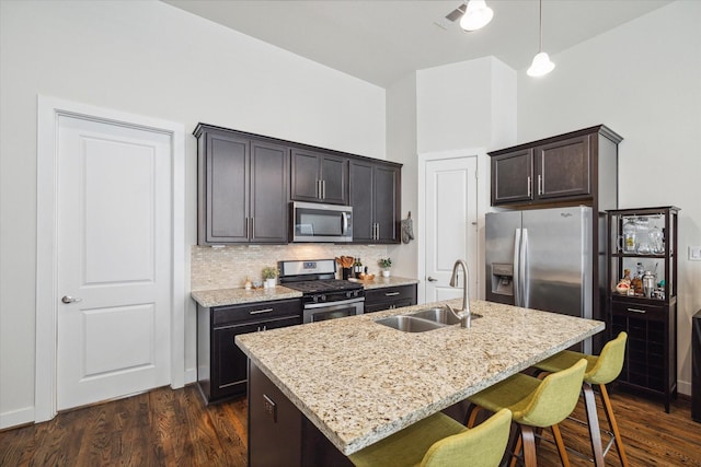 kitchen featuring pendant lighting, an island with sink, sink, dark brown cabinetry, and stainless steel appliances