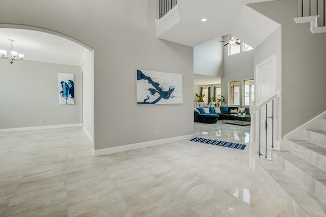 tiled foyer entrance featuring ceiling fan with notable chandelier and a high ceiling