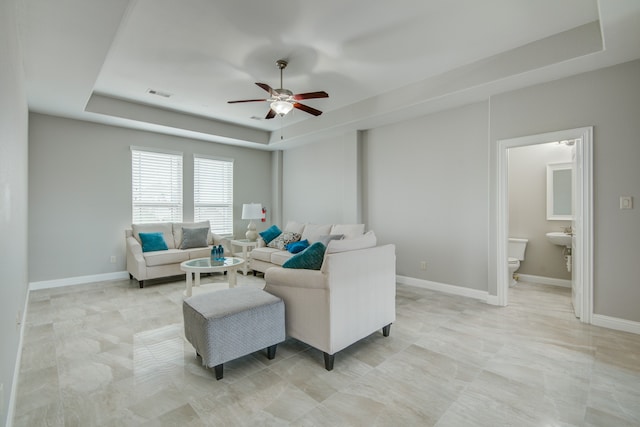 living room featuring ceiling fan, light tile patterned flooring, and a tray ceiling