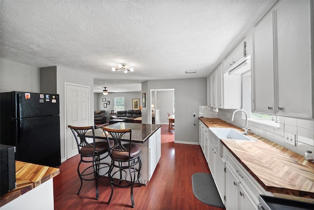 kitchen with sink, black fridge, white cabinetry, a kitchen breakfast bar, and a kitchen island