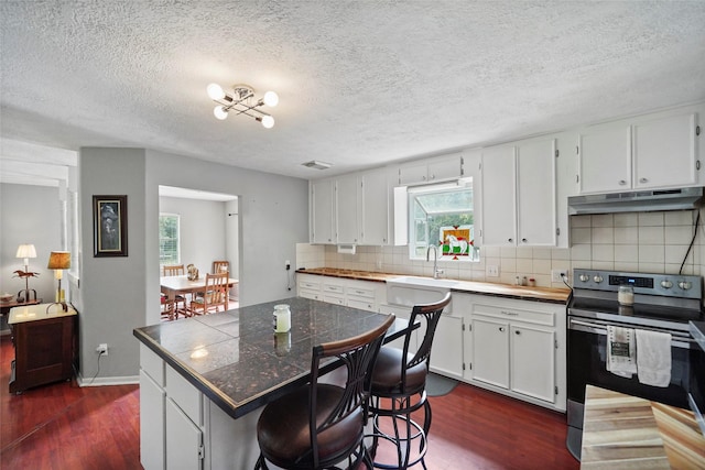 kitchen with a breakfast bar, white cabinets, a center island, dark wood-type flooring, and electric stove