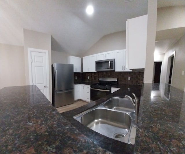 kitchen with vaulted ceiling, appliances with stainless steel finishes, sink, white cabinetry, and dark stone counters