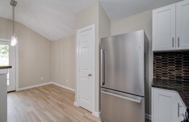 kitchen featuring stainless steel refrigerator, white cabinets, dark stone countertops, pendant lighting, and vaulted ceiling