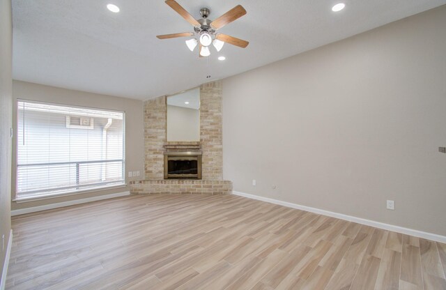 unfurnished living room featuring vaulted ceiling, a brick fireplace, light hardwood / wood-style flooring, and ceiling fan