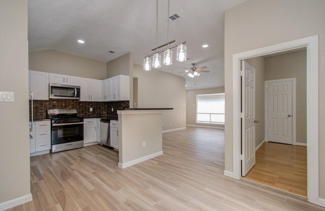 kitchen featuring white cabinets, decorative light fixtures, stainless steel appliances, kitchen peninsula, and vaulted ceiling