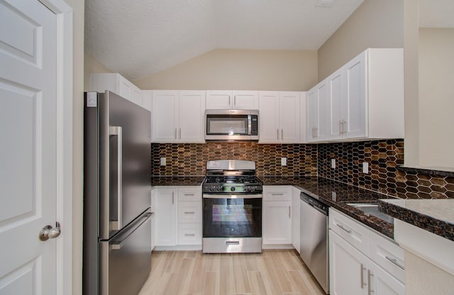 kitchen featuring white cabinetry, dark stone counters, decorative backsplash, lofted ceiling, and stainless steel appliances