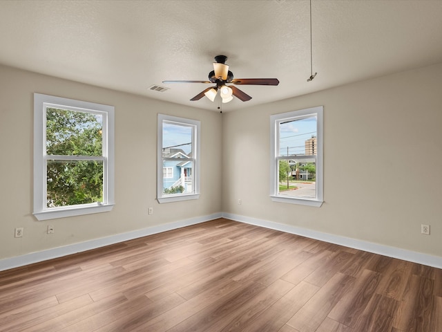 unfurnished room featuring ceiling fan, a wealth of natural light, wood-type flooring, and a textured ceiling