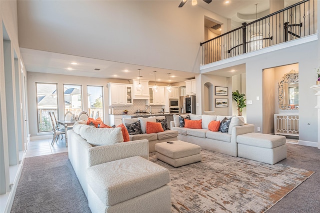 carpeted living room with ceiling fan, sink, and a towering ceiling