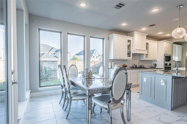 kitchen featuring appliances with stainless steel finishes, a center island with sink, dark stone countertops, white cabinets, and hanging light fixtures