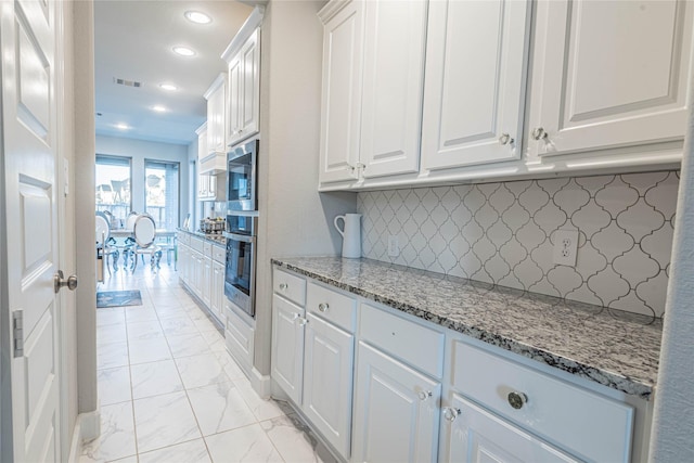 kitchen featuring decorative backsplash, white cabinetry, and light stone countertops