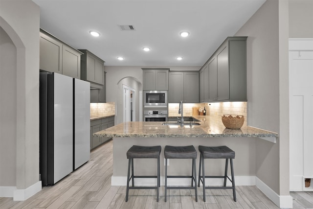 kitchen with kitchen peninsula, appliances with stainless steel finishes, gray cabinetry, sink, and light hardwood / wood-style floors