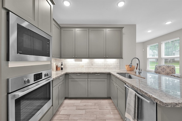 kitchen featuring kitchen peninsula, light stone countertops, sink, and appliances with stainless steel finishes