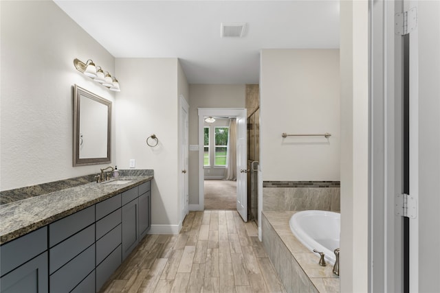 bathroom with vanity, hardwood / wood-style flooring, and tiled tub