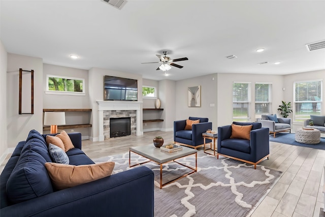 living room with a stone fireplace, a wealth of natural light, ceiling fan, and light wood-type flooring