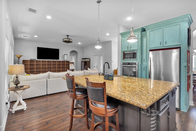 kitchen featuring stainless steel appliances, sink, hanging light fixtures, a kitchen island with sink, and dark wood-type flooring