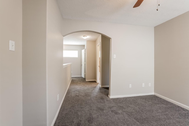 empty room featuring ceiling fan, a textured ceiling, and dark colored carpet