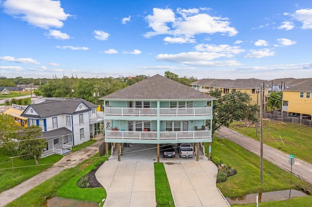 rear view of house featuring roof with shingles, a yard, concrete driveway, a balcony, and a residential view