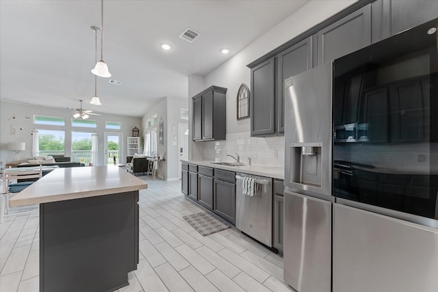 kitchen with decorative backsplash, ceiling fan, decorative light fixtures, a kitchen island, and stainless steel appliances