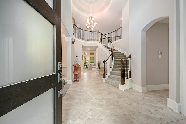 tiled entrance foyer featuring a raised ceiling, a notable chandelier, and a towering ceiling