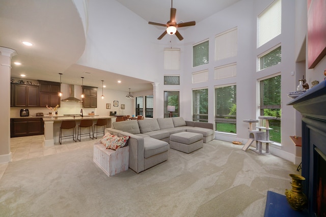 living room featuring decorative columns, light carpet, ceiling fan, and a towering ceiling