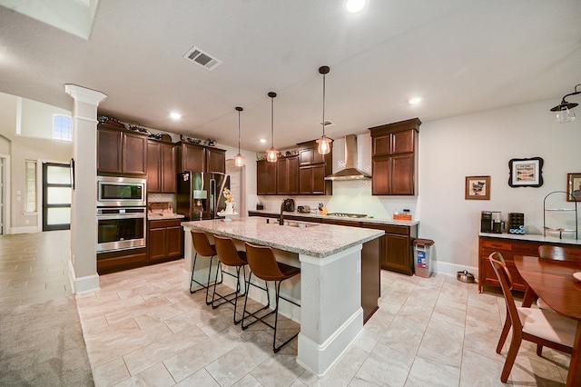 kitchen with decorative light fixtures, stainless steel appliances, wall chimney exhaust hood, a kitchen breakfast bar, and a kitchen island with sink