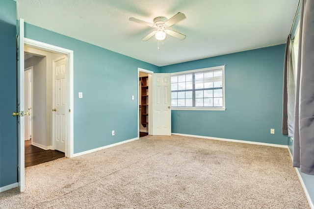 unfurnished bedroom featuring carpet, a walk in closet, a closet, and ceiling fan