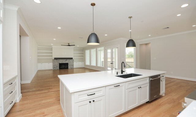 kitchen with sink, an island with sink, a fireplace, hanging light fixtures, and white cabinets